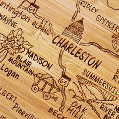 Close-up of the Totally Bamboo 4-Piece West Virginia Puzzle Coaster Set with Case, featuring a laser-engraved map of West Virginia's cities and landmarks. Notable details include an illustration of the State Capitol in Charleston, a mining cart near Blair Mountain, and place names like Madison and Saint Albans—ideal for unique coaster gifts.