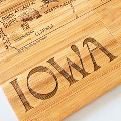 Presenting the 4-Piece Iowa Puzzle Coaster Set with Case crafted by Totally Bamboo, this unique wooden board showcases a laser-engraved map of Iowa, highlighting cities such as Council Bluffs, Atlantic, and Red Oak. The word "IOWA" is prominently featured in large letters.