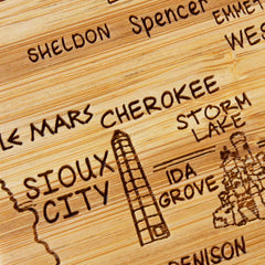 The 4-Piece Iowa Puzzle Coaster Set with Case by Totally Bamboo features a wooden map with engraved names of towns and landmarks, such as "Sioux City," "Storm Lake," "Cherokee," and "Ida Grove." The set's simple illustrations, including a building near Sioux City, offer a unique blend of art and utility.