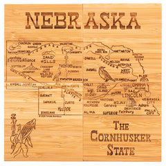 This 4-piece Nebraska Puzzle Coaster Set with Case from Totally Bamboo, perfect for a gift set, displays a detailed map of Nebraska. It highlights cities and landmarks with charming illustrations of corn and a bird. The set is labeled "Nebraska" at the top and "The Cornhusker State" at the bottom, making it a keepsake to cherish.