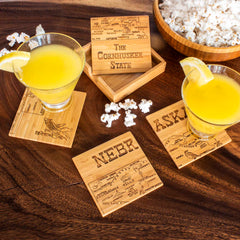 Nebraska map and attractions artwork engraved across 4 square bamboo coasters with storage case, cocktails and snacks on dark wooden table