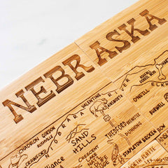 Close-up of a 4-piece Nebraska puzzle coaster set with case, crafted by Totally Bamboo, perfect as part of a gift set. Each coaster highlights cities like Omaha, Lincoln, and the Sand Hills with decorative lettering.