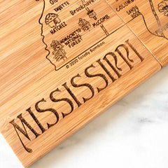 The 4-Piece Mississippi Puzzle Coaster Set with Case by Totally Bamboo doubles as a laser-engraved artwork, showcasing an intricate map of Mississippi complete with city names and landmarks such as the Homochitto National Forest. The word "MISSISSIPPI" is engraved in a large, decorative font at the bottom, adding charm to this unique piece.