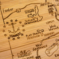 A detailed close-up of the 4-Piece Rhode Island Puzzle Coaster Set with Case by Totally Bamboo reveals its laser-engraved wooden design, featuring intricate details of towns and landmarks in a hand-drawn style. It showcases notable elements like an anchor symbol labeled "Hope," Scituate Reservoir, Flat River Reservoir, and towns like Coventry and West Warwick, making it a unique addition to any coaster collection.