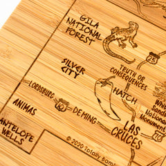 Close-up of a Totally Bamboo laser-engraved wooden coaster from the 4-piece New Mexico Puzzle Coaster Set with Case, showcasing locations like Gila National Forest, Truth or Consequences, Hatch, Silver City, Lordsburg, Deming, Las Cruces, and Animas. The coaster is uniquely adorned with illustrations of a lizard and pepper for added charm.