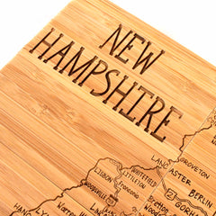 Explore a distinctive gift with this intricately detailed wooden carving of a laser-engraved map of New Hampshire. Crafted by Totally Bamboo, the design features city names such as Berlin and Lancaster, along with "NEW HAMPSHIRE" prominently displayed at the top, echoing the artistry of the 4-Piece New Hampshire Puzzle Coaster Set with Case masterpiece.