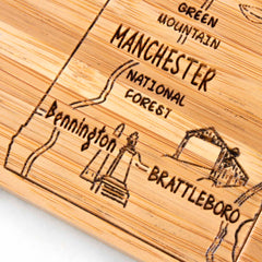 The 4-Piece Vermont Puzzle Coaster Set with Case by Totally Bamboo features a wooden map with engraved locations in Vermont, including Manchester, the Green Mountain National Forest, and towns such as Bennington and Brattleboro. This distinctive coaster set includes simplistic illustrations beside each name for an added charming touch.