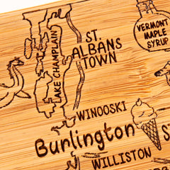 A close-up showcases the Totally Bamboo 4-Piece Vermont Puzzle Coaster Set with Case, featuring a laser-engraved wooden board map of Vermont highlighting towns such as St. Albans and Burlington. The set includes unique illustrations like an ice cream cone and the text "Vermont maple syrup," making it both functional and decorative.