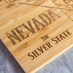 The 4-Piece Nevada Puzzle Coaster Set with Case by Totally Bamboo showcases a distinctive design, featuring a detailed laser engraving of "Nevada" and "The Silver State" on a finely textured, light-finished wooden surface. Subtle elements of the map, such as "Lake Tahoe," are artfully incorporated into the background.