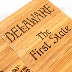 The "4-Piece Delaware Puzzle Coaster Set with Case" by Totally Bamboo features the words "DELAWARE The First State" beautifully etched in a stylized font, highlighting the natural wood grain. This set captures the same artisanal charm as our bamboo cutting board.