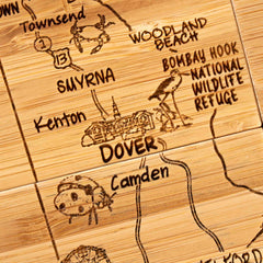 The 4-Piece Delaware Puzzle Coaster Set with Case by Totally Bamboo features a carved wooden map highlighting locations in Delaware like Townsend, Smyrna, Dover, Woodland Beach, and Camden. This set also includes laser-engraved icons such as a crab, a bird from Bombay Hook National Wildlife Refuge, and a building from Dover.