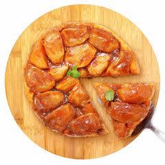 A caramelized apple tart is elegantly displayed on the TB Home® 14" Lazy Susan Turntable by Totally Bamboo, with its full 360-degree rotation. A slice is being taken using a metal spatula, while a small mint sprig graces the top, making it an ideal piece for improving kitchen organization.