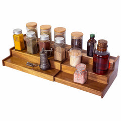 The TB Home® 3-Tier Expandable Spice Rack by Totally Bamboo elegantly displays an array of glass jars containing spices, herbs, and seeds. This tiered organizer includes a combination of bottles, corked jars, and a vintage-style pepper grinder for ideal spice storage.