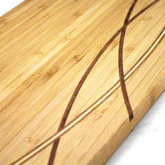 A close-up of the Del Mar Extra-Large Charcuterie Board by Totally Bamboo showcases its smooth, light moso bamboo surface with two dark, curved, intersecting lines as a design. The dimensions of the board are 30" x 8-1/2".