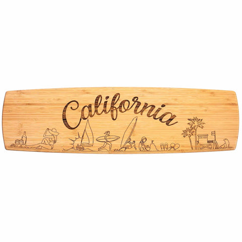 The Totally Bamboo California Engraved XL Charcuterie Board, measuring 30" x 8-1/2", features "California" elegantly laser-engraved in script. Below, line drawings depict beach scenes with surfers, umbrellas, sailboats, and palm trees—ideal for serving charcuterie with a coastal flair.