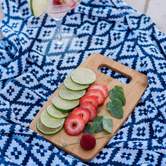 Limes, strawberries, and mint leaves are artistically arranged on a board from the 3-Piece Cutting Board Set by Totally Bamboo, set atop a blue patterned cloth. Nearby, a glass containing a refreshing drink adorned with lime garnishes enhances the vibrant scene.