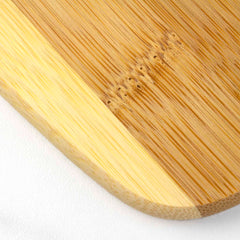 A close-up of a cutting board from Totally Bamboo's 3-Piece 2-Tone Cutting Board Set showcases the smooth, light grain pattern of Moso bamboo. The rounded corner highlights its natural texture and color variations. Resting elegantly on a white surface, this piece combines functionality with its appealing two-tone design.