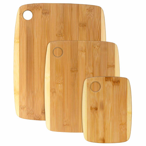 Introducing the 3-Piece 2-Tone Cutting Board Set from Totally Bamboo, comprising three nested boards of different sizes. Each board features a circular hole in the upper left corner and is crafted from Moso bamboo, displaying a light brown natural wood grain that enhances their two-tone design.