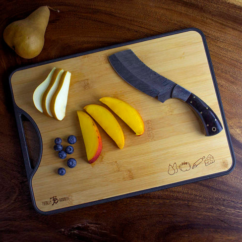 A "Poly-Boo" Reversible Bamboo/Plastic Cutting Board by Totally Bamboo displays a black-handled knife on its right side. On the left, sliced pears, mango pieces, and blueberries are arranged. A whole pear sits elegantly nearby on the bamboo surface.