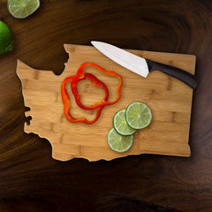 A Totally Bamboo Washington Cutting Board, measuring 15-1/2" x 10", features an arrangement of sliced red bell pepper and lime. Next to the vivid vegetables, a white knife with a black handle lies on the dark wooden surface, enhancing the appeal of this distinctive cutting board.