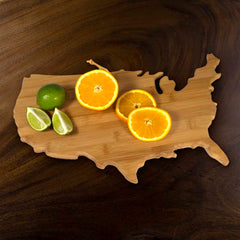 The Totally Bamboo USA Cutting Board, measuring 17-1/2" x 11", elegantly displays two whole green limes, two lime wedges, and two round orange slices on a dark surface.