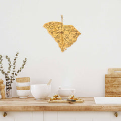 A kitchen counter adorned with white bowls, snacks, and wooden utensils on a light wooden surface. Above the counter, a Totally Bamboo Destination South Carolina Cutting Board (14" x 11-1/2") hangs on a white wall, its intricate laser-engraved design perfectly complementing the cozy ambiance.