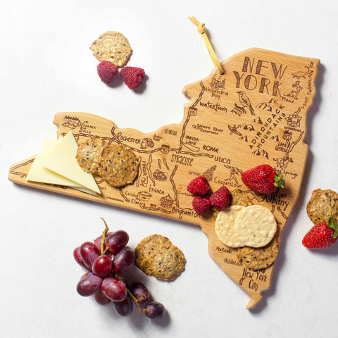 The Destination New York Cutting Board by Totally Bamboo, measuring 13-1/4" x 12", is beautifully arranged with cookies, crackers, raspberries, strawberries, cheese slices, and a bunch of grapes. Laser-engraved artwork intricately showcases landmarks and place names throughout the state of New York.