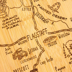 The "Destination Arizona" cutting board by Totally Bamboo, measuring 13-1/2" x 11-3/4", presents an intricately laser-engraved map of the state. Featuring locations like Flagstaff, Sedona, and the Grand Canyon National Park, it also includes playful designs such as a vintage car, cactus, and the Painted Desert.