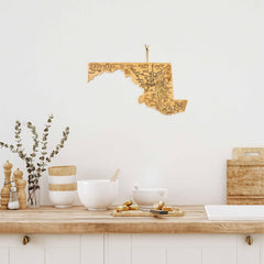 A kitchen featuring a warm wooden countertop and the Destination Maryland Cutting Board by Totally Bamboo serves bowls, jars, salt and pepper grinders, and eucalyptus stems. Above, a decorative map of Florida wall art adds character to the space.