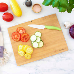 A Destination Colorado Cutting Board from Totally Bamboo, measuring 14-1/2" x 10-3/4", showcases sliced tomatoes, zucchini, and yellow squash beside a knife. The vibrant veggies are surrounded by garlic, onion, basil, and a salt shaker on a marble countertop.