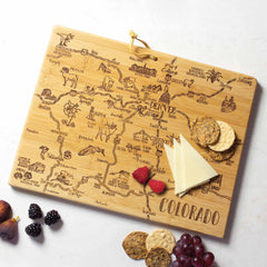 The Totally Bamboo Destination Colorado Cutting Board, measuring 14-1/2" x 10-3/4", features an engraved map highlighting cities and landmarks of Colorado. This state-shaped wooden board is perfect for displaying an assortment of cheeses, crackers, and fruits such as raspberries, blackberries, figs, and grapes, combining style with practicality.