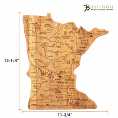 This board is a wooden cutting surface in the shape of Minnesota, featuring engraved illustrations of cities, landmarks, and symbols. It is part of Totally Bamboo's Destination Series and measures 13-1/4 inches by 11-3/4 inches, with the brand name subtly displayed in the corner.