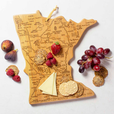 The Destination Minnesota Cutting Board, measuring 13-1/4" x 11-3/4" and crafted by Totally Bamboo, features city names and boasts a bamboo cutting surface adorned with cheese, crackers, figs, grapes, and strawberries.