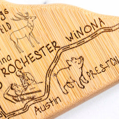 As a part of Totally Bamboo's Destination Minnesota Series, this cutting board measures 13-1/4" x 11-3/4" and showcases an engraved map with a route connecting Rochester, Winona, and Preston. It also features delightful illustrations of a deer, a fish, and a bear.