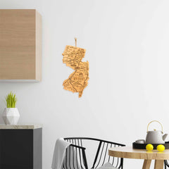 In a modern kitchen, a Totally Bamboo Destination New Jersey Cutting Board adorns a white wall. Beside it, a black chair is placed near the countertop where you can find a potted plant and another bamboo cutting board, adding to the decor. A fruit bowl and kettle sit on the counter, enhancing the minimalist atmosphere.