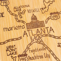 The Totally Bamboo Destination Georgia Cutting Board, measuring 11-3/4" x 13-1/4", features a laser-engraved wooden map highlighting parts of Georgia, including an illustration of a domed building to represent Atlanta. This intricately designed board also details Marietta, Roswell, Fayetteville, and Peachtree City along highways 75 and 85.