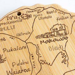 This Totally Bamboo Destination Maui Cutting Board features a laser-engraved wooden map highlighting Hawaiian towns such as Makawao and Olinda. It includes the winding Huelo Road and a detailed building illustration. A hanging hole at the top allows for easy display of this unique creation, sized at 15-1/2" x 9-1/8".