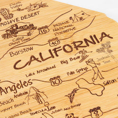 Discover the intricately laser-engraved Totally Bamboo Destination California Cutting Board, measuring 11" x 14-/4". This detailed wooden map highlights California's cities and landmarks, such as Los Angeles, Mojave Desert, Joshua Tree, and Death Valley. It features iconic symbols for beaches, national parks, and historical sites on a state-shaped bamboo surface that serves as both an artistic display piece and a functional cutting board.