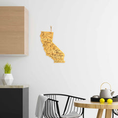 A modern kitchen showcases a geometric plant pot and a wall-mounted wooden map of California. On the round table, you'll find a teapot, lemons, and the "Destination California" Cutting Board by Totally Bamboo, paired with a black and white chair nearby. Minimalist decor featuring laser-engraved artwork and light colors contributes to the fresh ambiance.