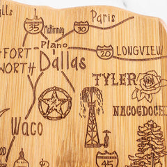 The Totally Bamboo Destination Texas Cutting Board, measuring 14" x 13-3/8", is uniquely shaped like the Lone Star State and showcases city names like Dallas, Fort Worth, and Tyler. It also features designs such as highway signs, a rose, an oil derrick, and a cowboy boot—making it an ideal piece of Texas kitchen decor.