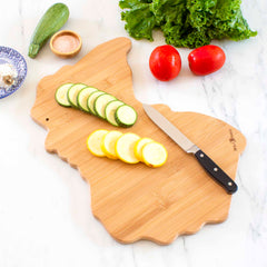 On a rabbit-shaped cutting board from Totally Bamboo's Destination Michigan series, sliced zucchini and squash are elegantly arranged with a knife resting beside them. Fresh lettuce, tomatoes, and a small bowl of salt complete the scene on the marble surface—perfect for your kitchen adventures.