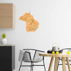 A modern, minimalist kitchen showcases black chairs and a round wooden table adorned with a tea set and lemons. The Destination Michigan Cutting Board by Totally Bamboo, measuring 16-3/4" x 16-1/2", is displayed on the wall near a geometric plant vase placed on the countertop. The space is bright and well-lit.