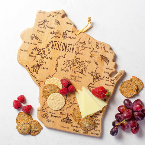 The Totally Bamboo Destination Wisconsin Cutting Board, measuring 12" x 13", features detailed laser-engraved artwork highlighting city names and landmarks across the state. It beautifully displays an arrangement of crackers, cheese slices, raspberries, and a bunch of grapes on a white surface.