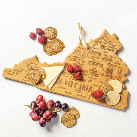 The Destination Virginia Cutting Board by Totally Bamboo, measuring 16-1/2" x 9-1/2", features a laser-engraved design of city names across its wooden surface. Elegantly arranged with slices of cheese, strawberries, raspberries, grapes, and crackers, it offers both functionality and charm. The state-shaped cutting board includes a twine loop for easy hanging, making it an attractive addition to any setting.