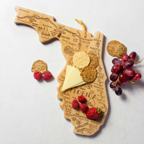 The Destination Florida Cutting Board by Totally Bamboo, measuring 13-1/2" x 12-1/4", is a beautifully crafted bamboo surface shaped like the state of Florida. It's laser-engraved with city names and holds cheese, crackers, strawberries, and grapes gracefully. This state-shaped cutting board also features decorative illustrations of palm trees and an orange.