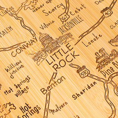 The Totally Bamboo Destination Arkansas Cutting Board, measuring 13" x 12", is crafted from bamboo and features engraved roads and cities across Arkansas. It prominently displays the State Capitol building in Little Rock and includes markings for nearby towns such as Benton, Conway, and Jacksonville along with the highways.