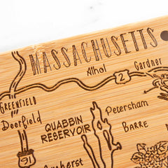 The Totally Bamboo Destination Massachusetts Cutting Board, measuring 16-3/4" x 9-1/4", features a laser-engraved map of Massachusetts highlighting towns including Athol, Gardner, and Greenfield. Landmarks like the Quabbin Reservoir are intricately detailed with roads artistically represented as flowing lines interlinking these areas.