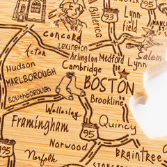 The Destination Massachusetts Cutting Board, measuring 16-3/4" x 9-1/4" by Totally Bamboo, is a wooden map designed in the shape of the state. It showcases town names around Boston like Concord, Lexington, and Cambridge. This laser-engraved artwork also features highways and a silhouette of Massachusetts.