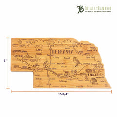 The Totally Bamboo Destination Nebraska Cutting Board, measuring 17-3/4 inches by 9 inches, features a bamboo cutting surface intricately shaped like the state of Nebraska. It is beautifully adorned with laser-engraved artwork that includes city names, landmarks, and images such as a windmill and crops.