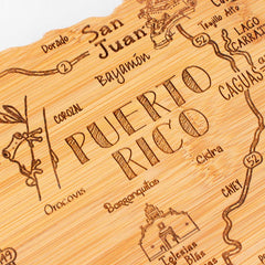 This elegant wooden carving from the Totally Bamboo Destination Series beautifully features a detailed map of Puerto Rico with town names such as San Juan and Bayamon engraved. Adorned with a coquí frog and church, the Destination Puerto Rico Cutting Board, 18" x 7", serves both as an exquisite charcuterie board and versatile bamboo cutting surface.